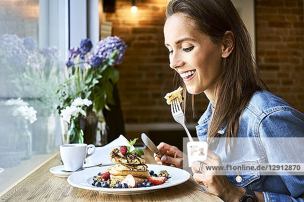 Smiling young woman eating pancakes in cafe