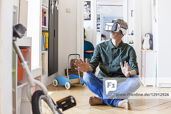 Mature man sitting on the floor at home using Virtual Reality Glasses