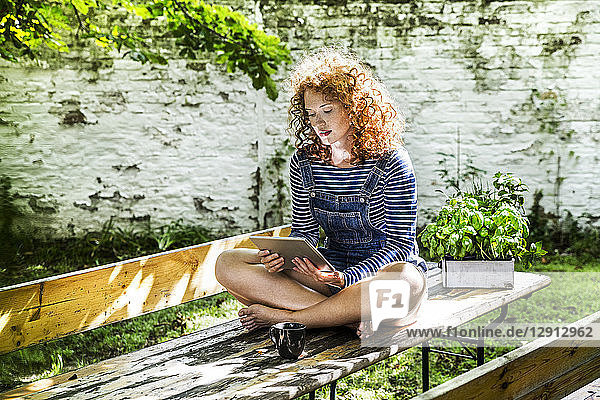 Portrait of young woman sitting on beer table in the garden using tablet