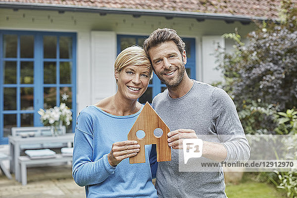 Portrait of smiling couple standing in front of their home holding house model