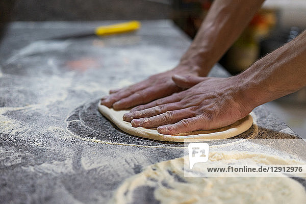 Close-up of pizza baker preparing pizza dough in kitchen