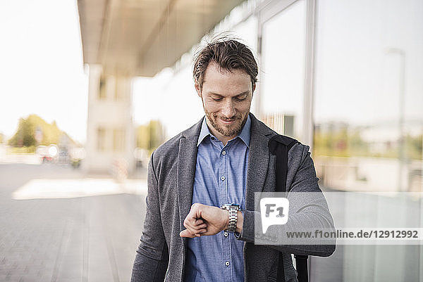 Smiling businessman with laptop bag checking the time