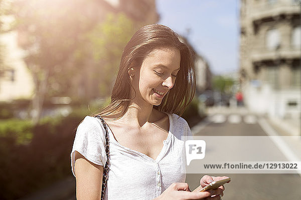 Smiling young woman looking at cell phone in the city