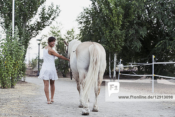 Smiling woman in white dress leading horse
