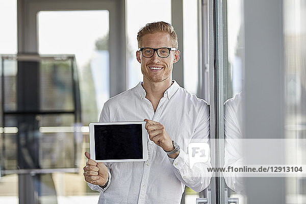 Portrait of smiling businessman showing tablet at the window in office
