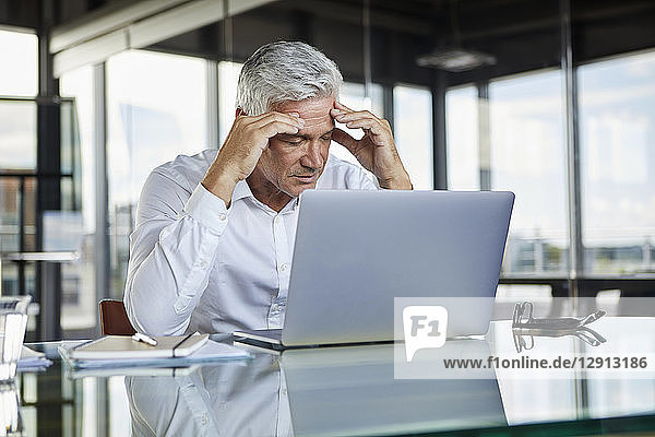 Stressed businessman sitting at desk with laptop  holding his head