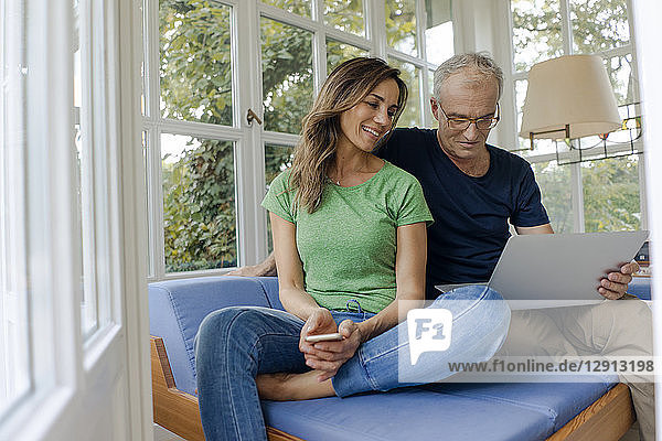 Smiling mature couple sitting on couch at home sharing laptop