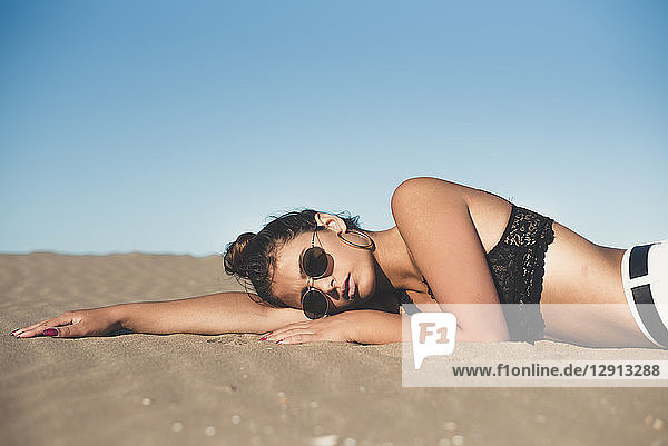 Portrait of teenage girl wearing sunglasses lying on sandy beach