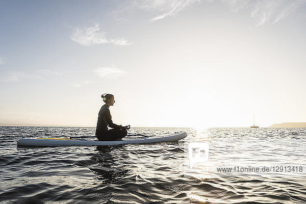 Young woman meditating on paddleboard at sunset