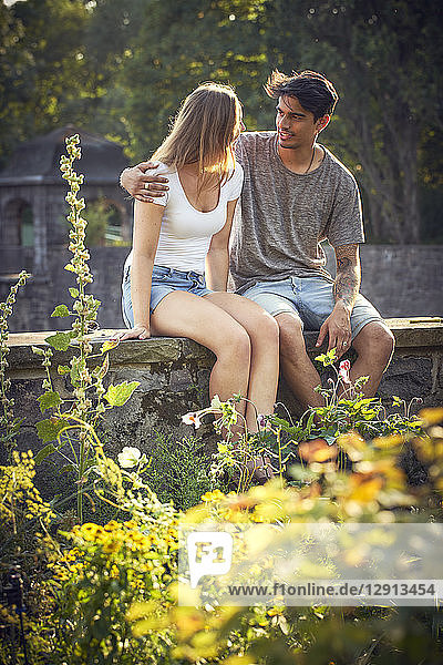 Romantic young couple sitting on wall in a park  with arms around