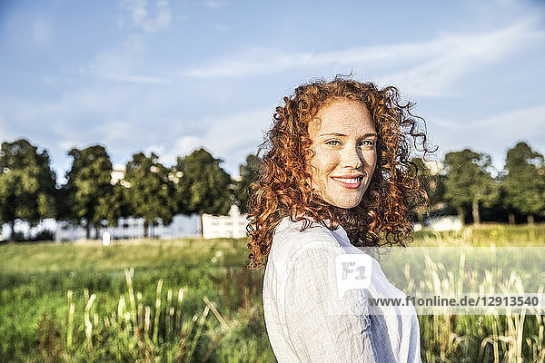 Germany  Cologne  portrait of smiling young woman with curly red hair in nature