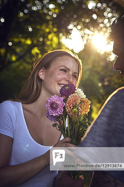 Young man meeting his girlfriend in a park,  gifting her with flowers