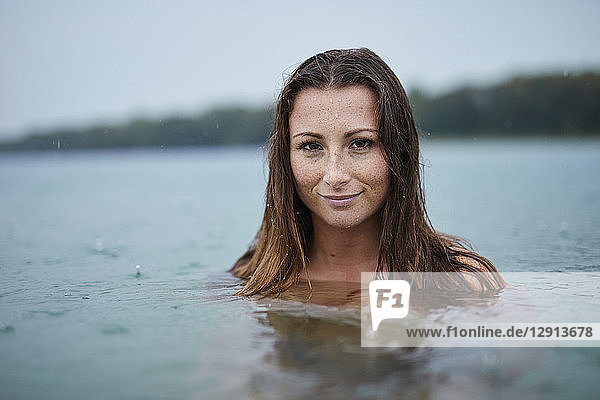 Portrait of freckled young woman bathing in lake on rainy day