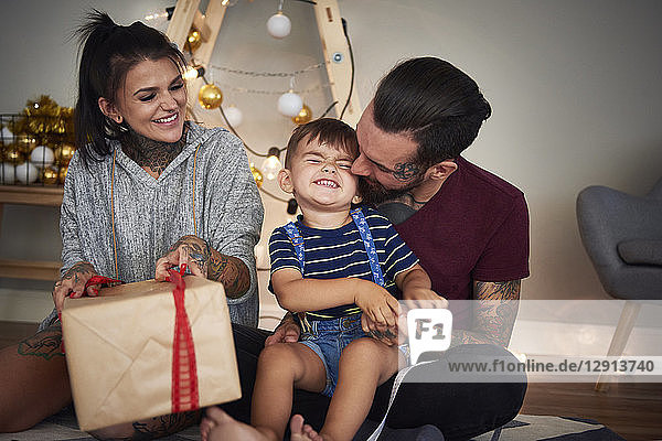 Happy boy opening Christmas present with his parents at home