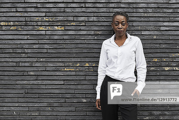 Portrait of smart businesswoman wearing white shirt and black trousers leaning against wall