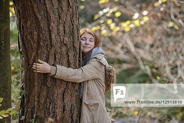 Portrait of smiling teenage girl hugging tree trunk in autumnal forest