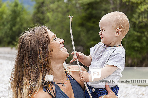 Smiling mother with baby boy holding a stick in the nature
