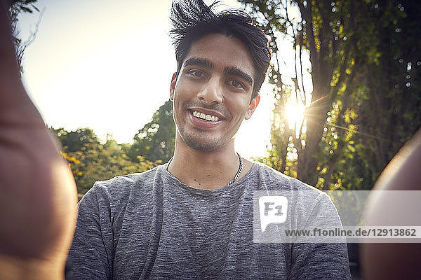 Portrait of a young man in a park at sunset,  taking selfie