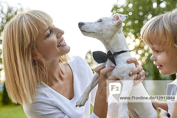 Happy woman with daughter holding dog wearing a bowtie outdoors
