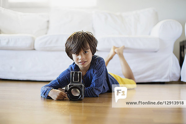 Portrait of boy lying on the floor at home with an old-fashioned film camera