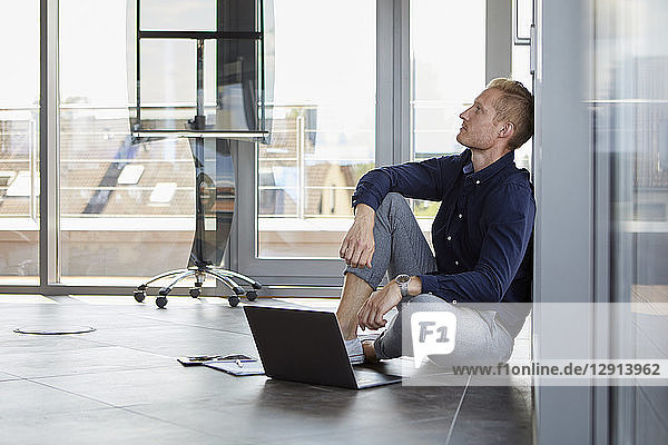Businessman sitting on the floor next to laptop