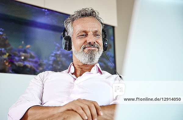 Businessman with headphones using laptop at desk in front of aquarium
