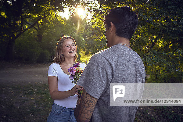 Young man meeting his girlfriend in a park  gifting her with flowers