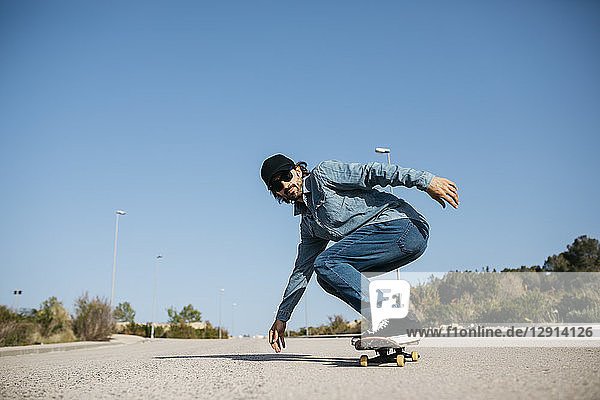 Trendy man in denim and cap skateboarding