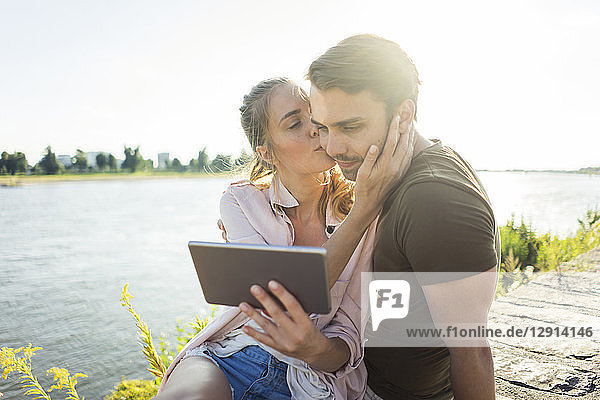 Couple kissing at the riverside in summer holding tablet