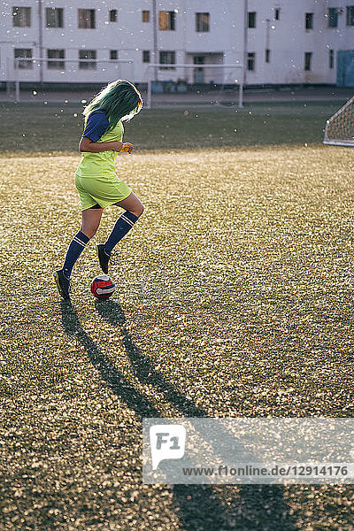 Young woman playing football on football ground dribbling with the ball