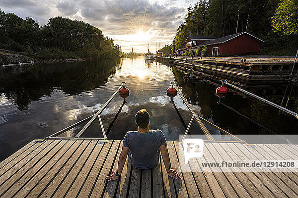 Finland  Kajaani  Man sitting on jetty  watching sunset  rear view