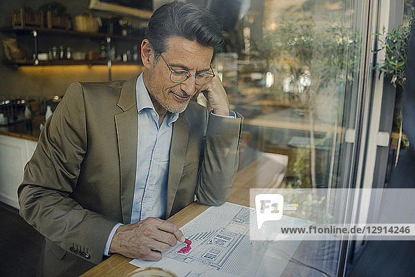 Mature businessman sitting in coffee shop  drawing outline of a house