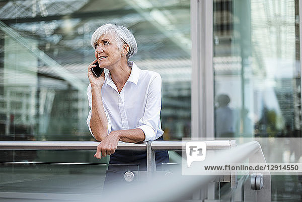 Senior businesswoman leaning on railing in the city talking on cell phone