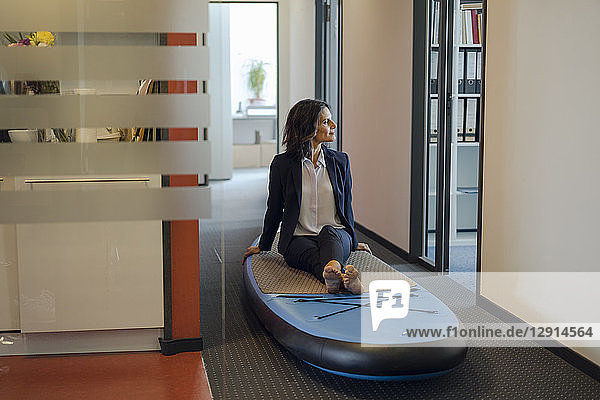 Businesswoman sitting on paddle board  daydreaming in office