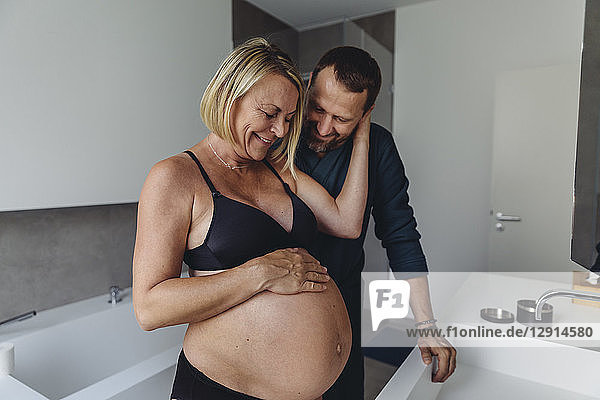 Happy mature pregnant couple watching expectant mother?s belly in bathroom