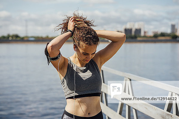 Young athletic woman wearing earbuds at the riverside making her hair