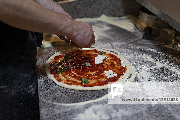 Close-up of pizza baker preparing a pizza with tomato sauce and mozzarella in kitchen