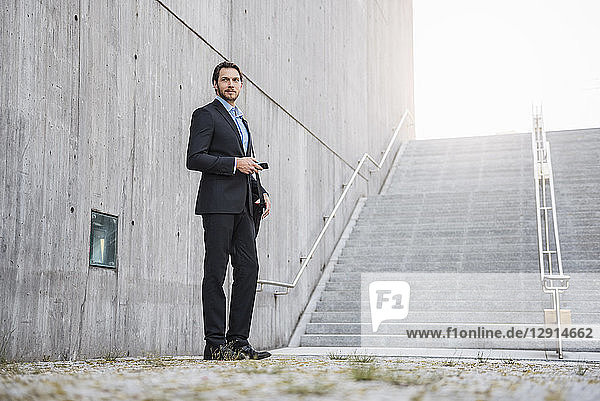 Businessman standing at stairs holding smartphone