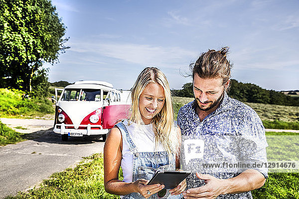 Happy couple outside van in rural landscape looking at tablet