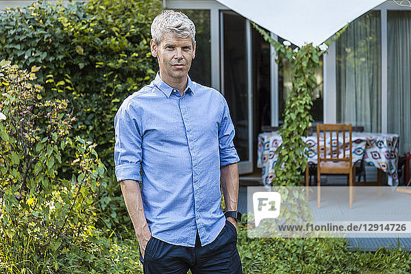 Portrait of mature man with grey hair standing in garden of his house