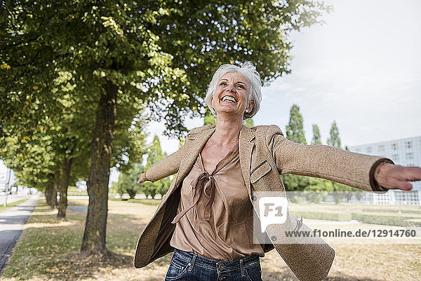 Happy senior woman with outstretched arms in a park