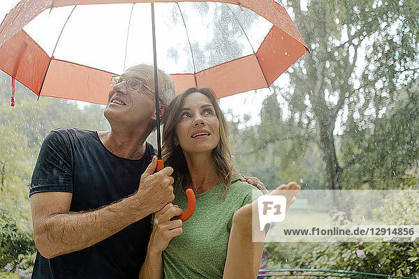 Smiling mature couple standing in rain under umbrella