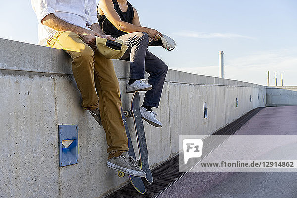 Close-up of two young men with skateboards sitting on a wall