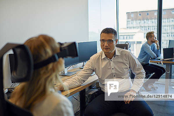 Man looking at woman wearing VR glasses in office