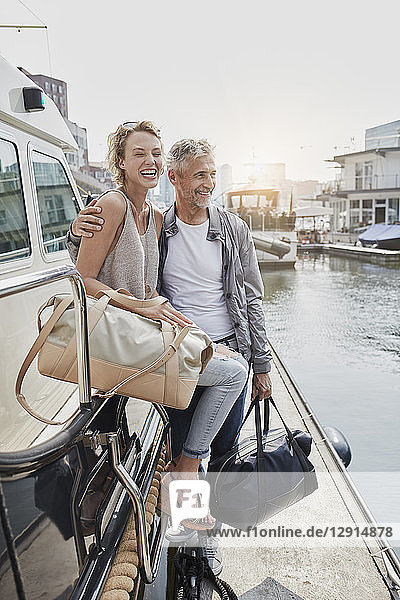 Older man and young woman standing with travelling bags on jetty next to yacht