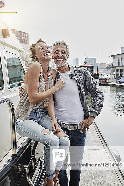 Laughing older man and young woman standing on jetty next to yacht