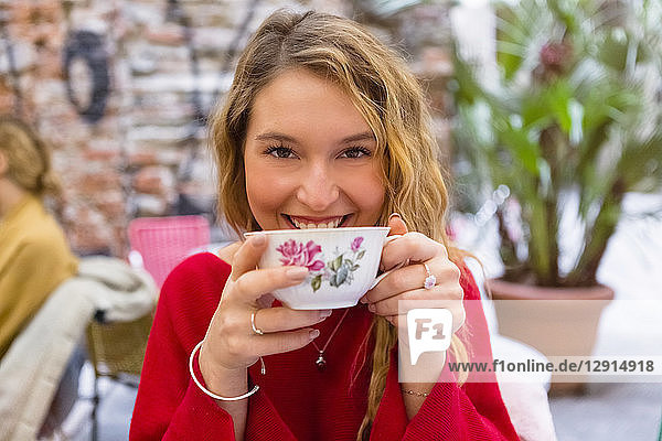 Portrait of smiling young woman drinking cup of tea at pavement cafe