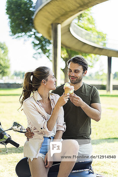 Smiling couple with motor scooter in summer eating ice cream