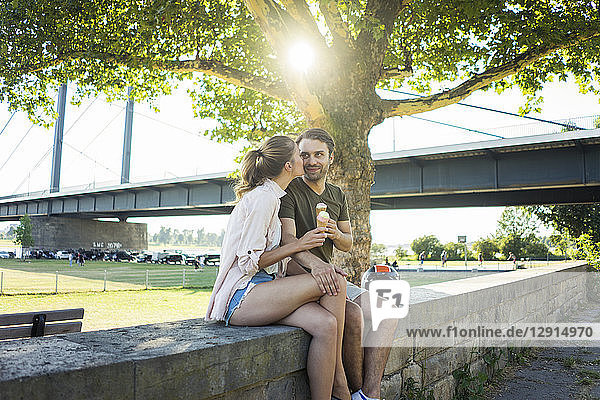 Happy couple sitting on a wall in summer eating ice cream