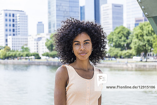 Germany  Frankfurt  portrait of relaxed young woman with curly hair in front of Main River